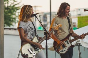 Woman Playing Guitar While Singing Beside Man Playing Bass Guitar Near Microphone